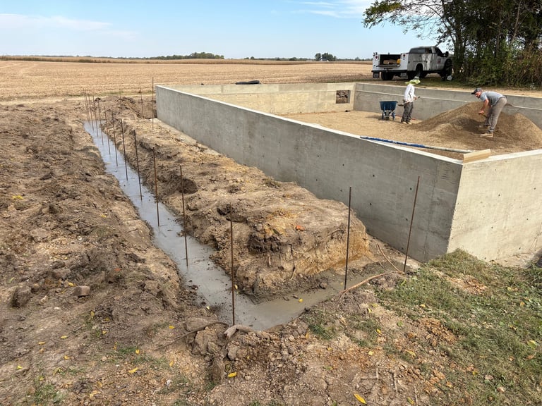 Agricultural basin and drainage ditch in rural farmland with equipment visible in background