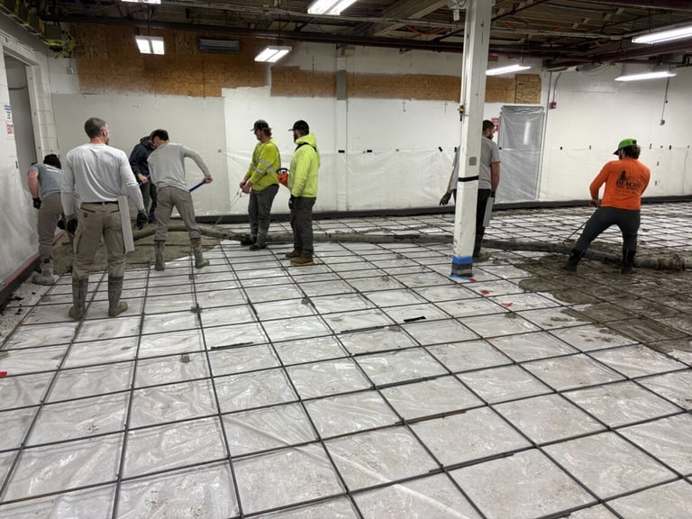 Construction workers in safety gear inspecting a large empty warehouse floor with a grid layout of tiles