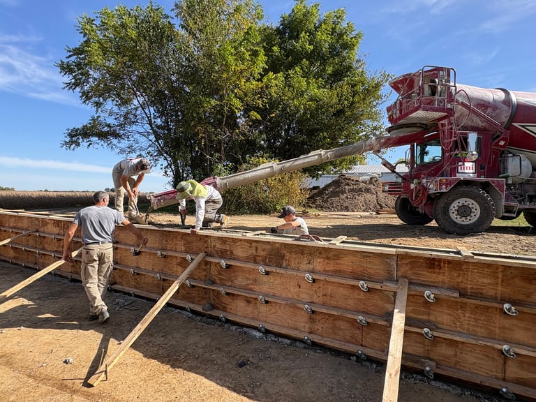 Workers loading wood chips into large wooden storage bins using an industrial chipping machine under clear blue skies
