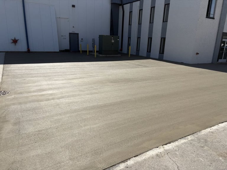 Empty concrete parking lot or loading area next to industrial building with white walls and metal doors