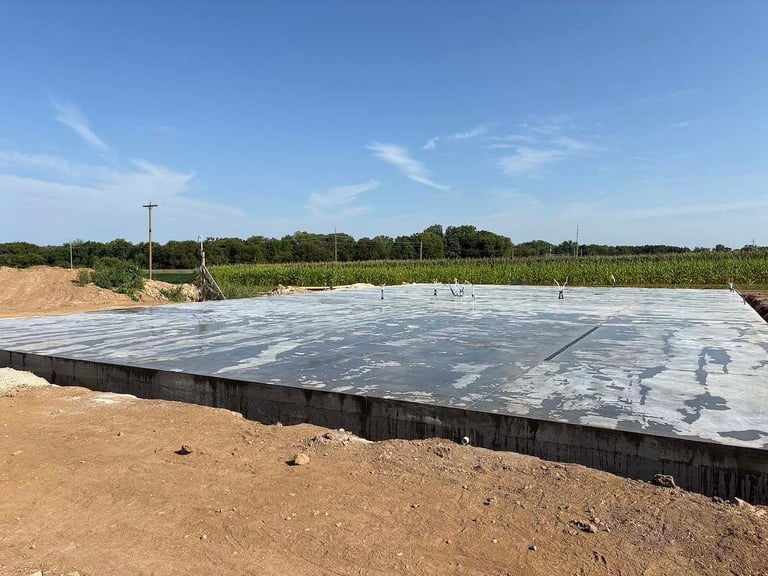 Concrete foundation or pad under construction in agricultural field with crops visible in background and clear blue sky