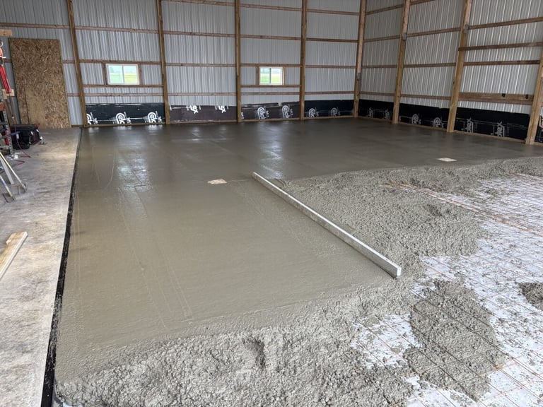 Concrete floor being poured and smoothed in a large metal warehouse interior with piles of gravel