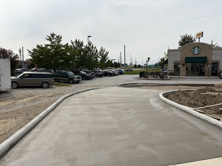 Newly paved parking lot with curved entrance, parked cars, trees, and Starbucks building in background