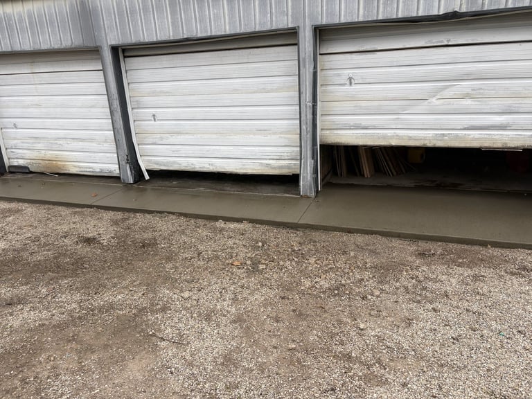 Three white garage doors on a metal building with concrete driveway below