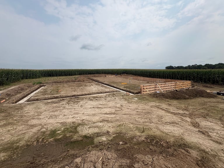 Cleared farmland with stacked lumber and green corn fields under cloudy sky