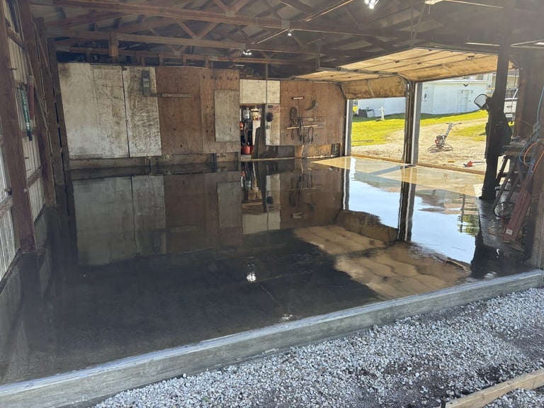 Empty industrial garage or storage facility with concrete floor, metal walls, and open doors showing rural landscape outside