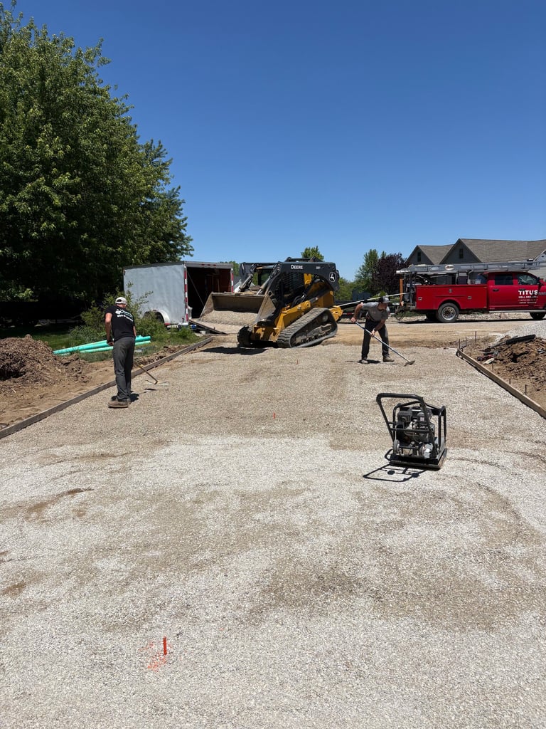 Construction site with workers, yellow track loader, red truck, and equipment on gravel ground under clear sky