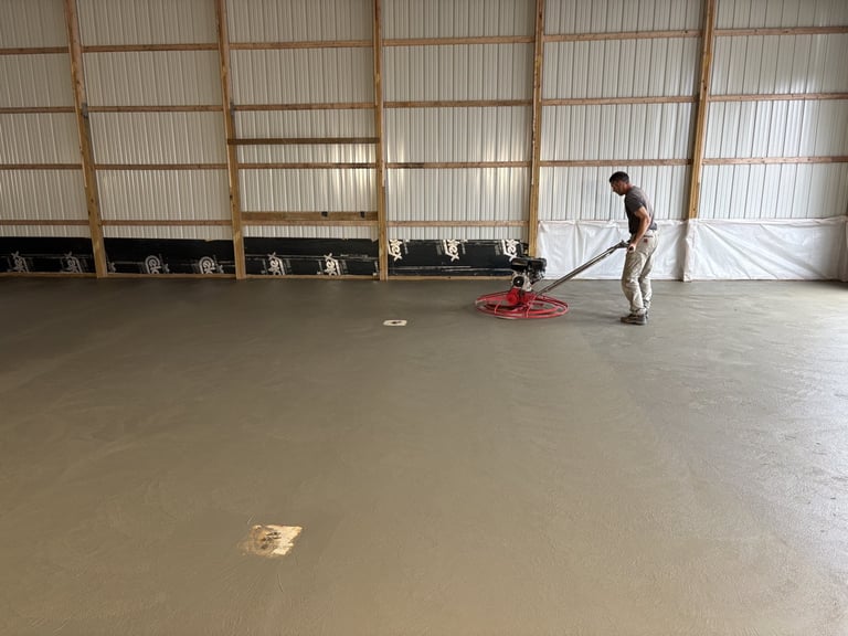 Worker finishing wet concrete floor in large industrial warehouse with corrugated metal walls