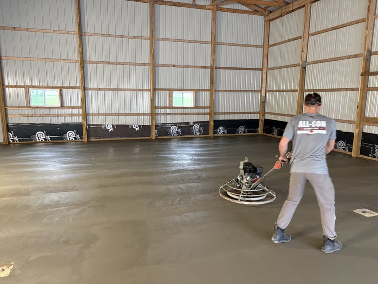 Worker using power trowel to finish concrete floor in industrial warehouse with metal framework and polycarbonate panels
