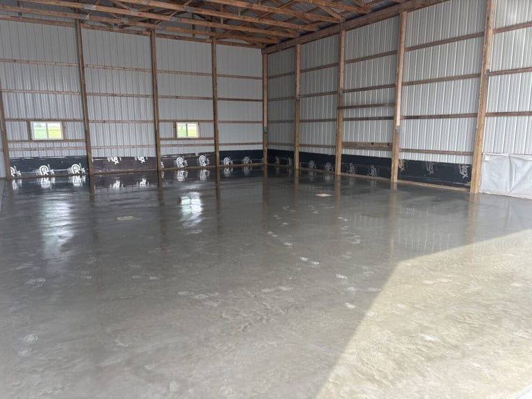 Empty warehouse or industrial building interior with concrete flooring, metal roof framework, and corrugated metal wall panels
