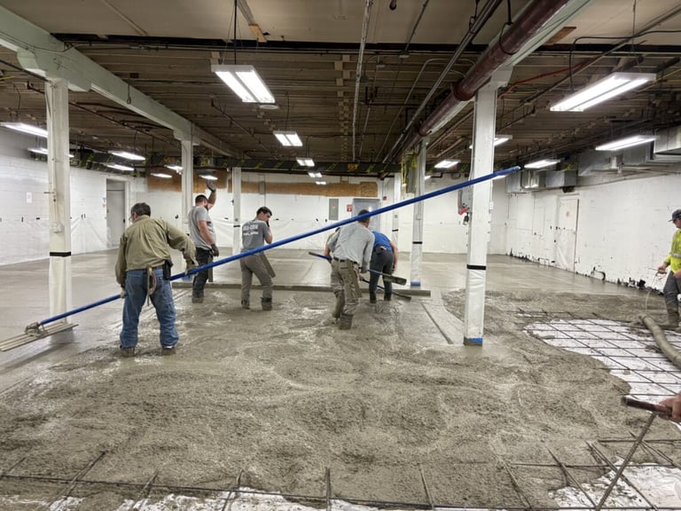 Workers pouring concrete in an industrial warehouse space with white columns and overhead lighting