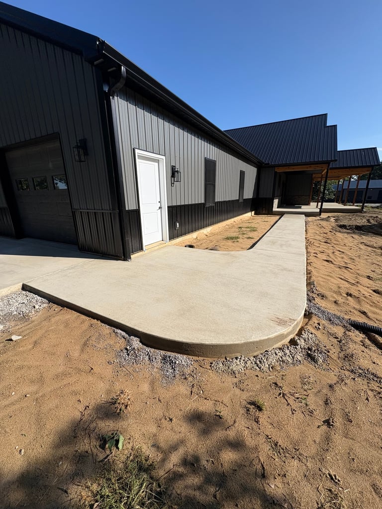 Modern black and white metal barn buildings with concrete entryway under construction on rural property
