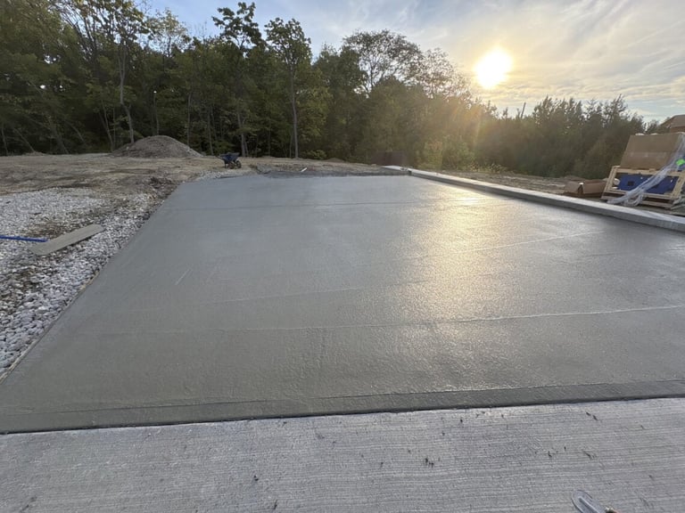 Newly poured concrete foundation or pool deck during sunset with surrounding trees and forest in background