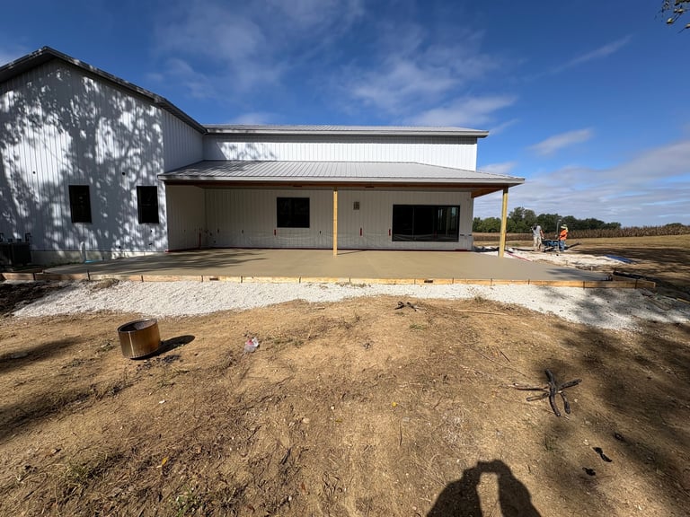 Modern metal warehouse building under construction on dirt foundation with clear blue sky, rural landscape background