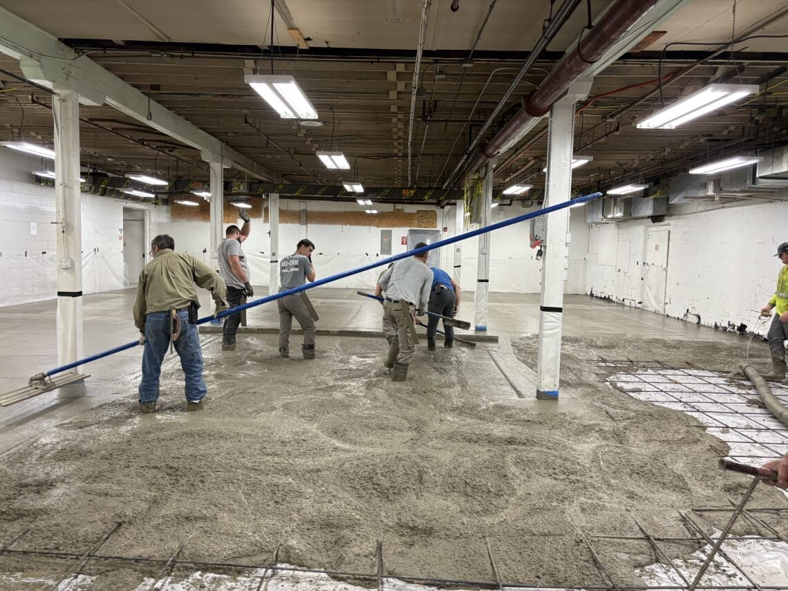 Workers leveling concrete in an industrial warehouse space with blue screed beam and exposed ceiling infrastructure