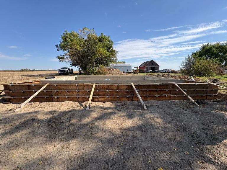 Wooden livestock feed trough or hay rack on rural farm with barn and fields in background under clear blue sky