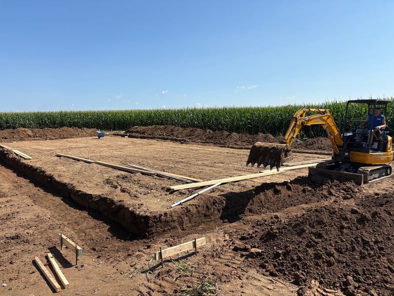 Yellow excavator working on agricultural land clearing and digging with cornfield in background under clear blue sky