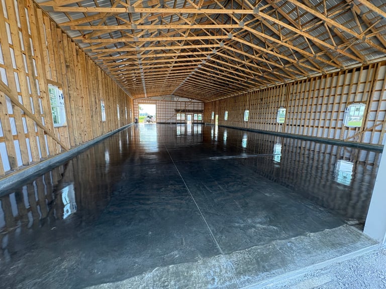 Interior of empty horse barn with wooden frame, dark asphalt floor, and metal roof beams