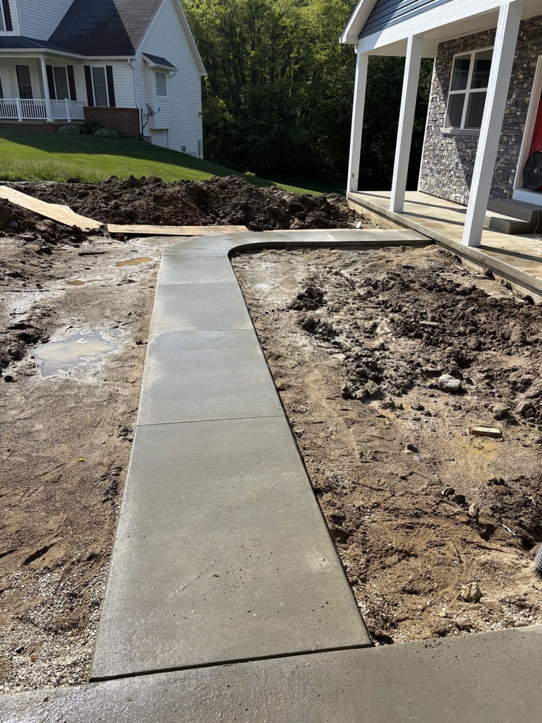 New concrete walkway being installed between landscaped areas next to a residential home with patio