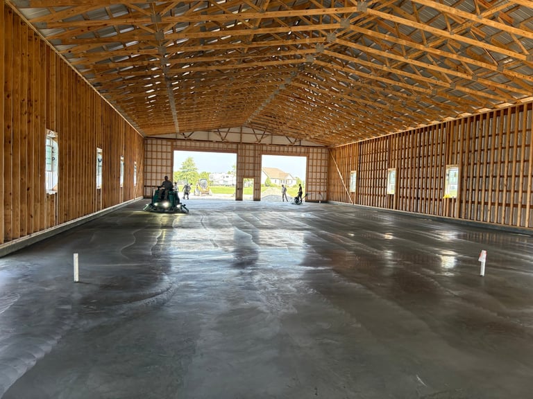 Empty rustic barn interior with wooden beams, polished concrete floor, and people near open doors